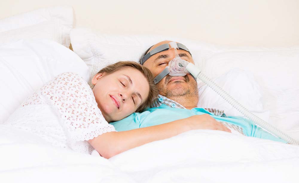 Woman asleep in bed next to man using sleep machine